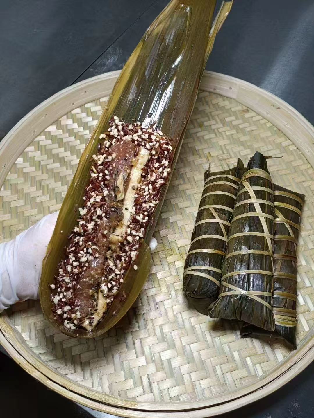竹蒸笼内打开的红黑米粽和三只完整粽子